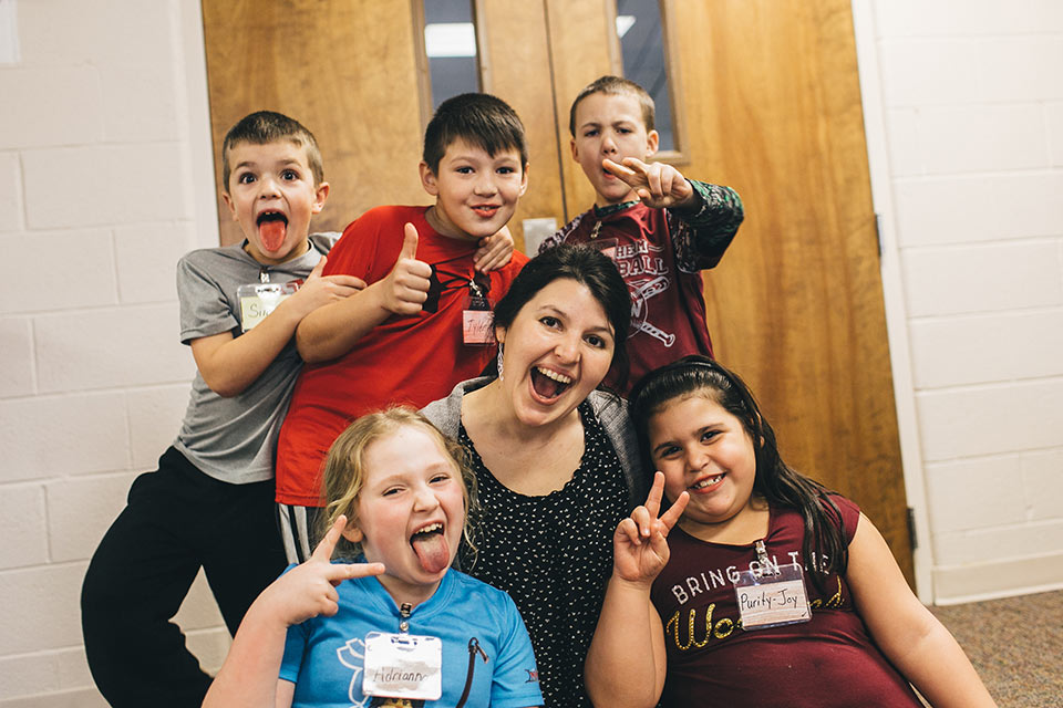 A group of kids surrounding a woman volunteer and smiling