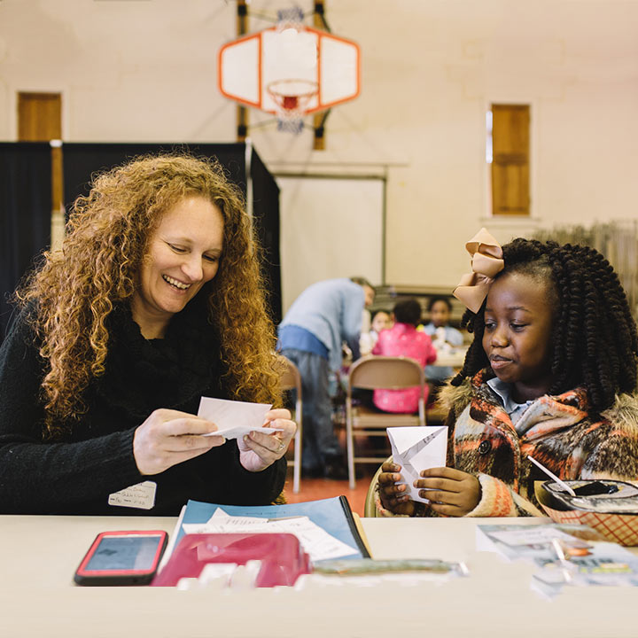 A woman and a young girl working on a craft together smiling