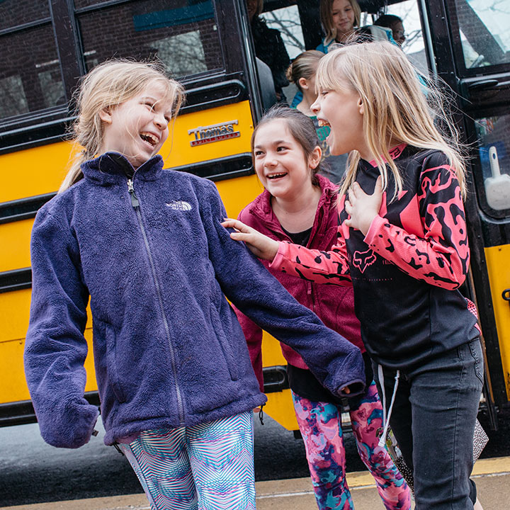 A group of 3 girls getting off of a school bus laughing together