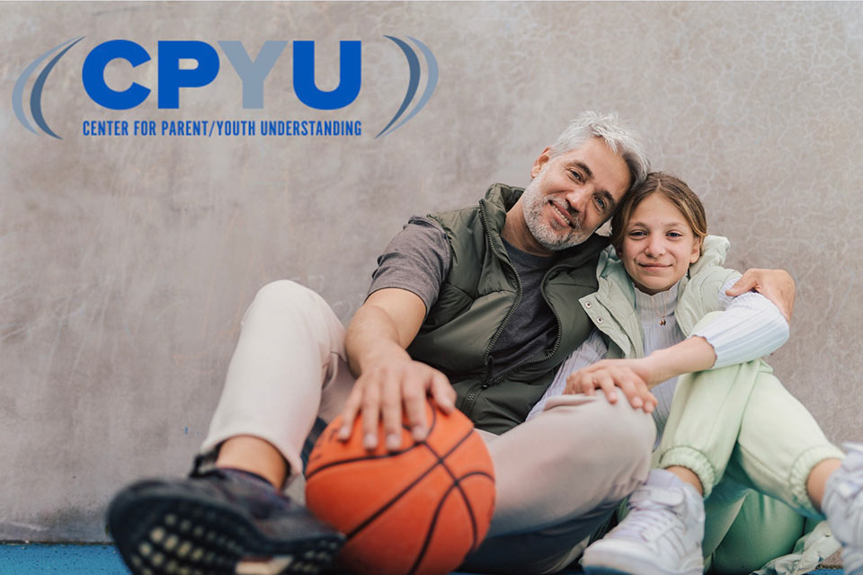 An image of a Dad and daughter sitting sise-by-side holding a basketball with the CPYU logo in the corner