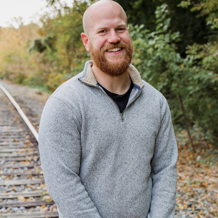 A picture of Kurt Zimmerman smiling at the camera while standing near railroad tracks