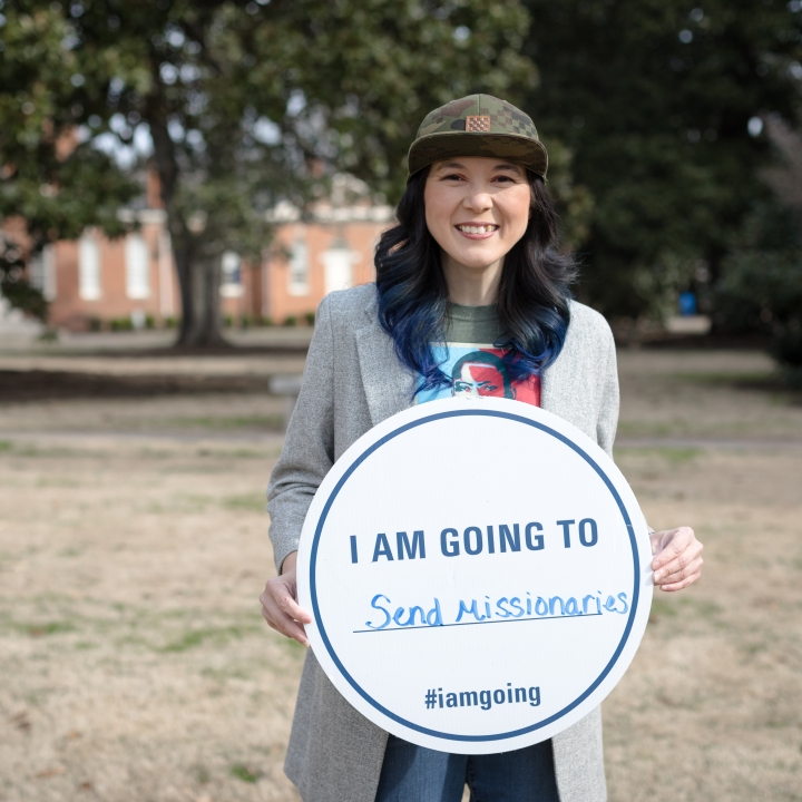 A picture of Megan Brown outside holding a sign that says I am going to send missionaries hashtag I am going